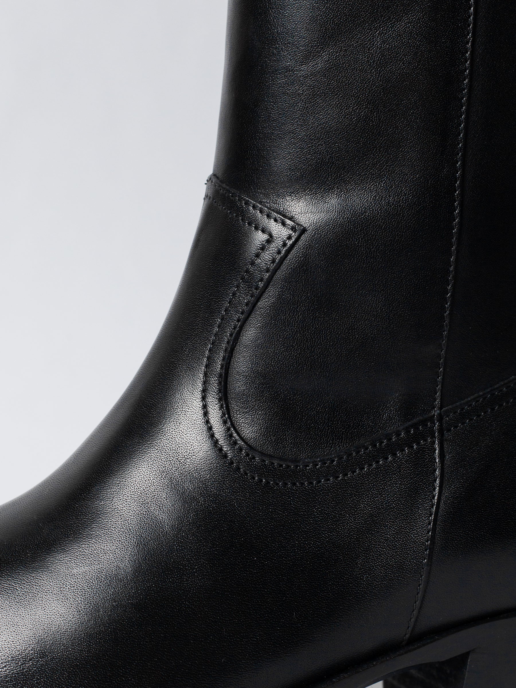 Close-up of a black leather boot with detailed stitching on a light gray background