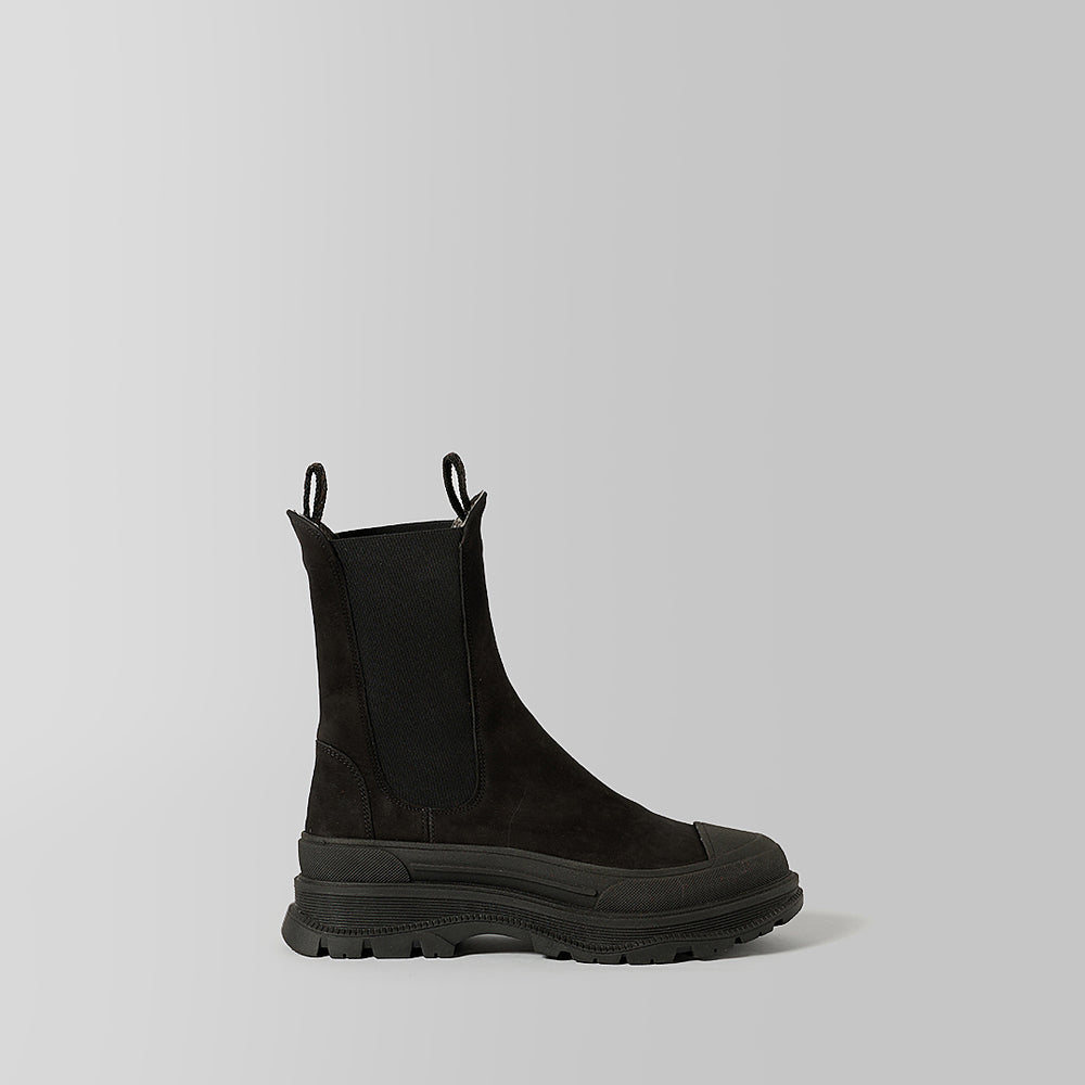 A single black Chelsea-style ankle boot with a chunky lug sole, side gusset, and pull tabs, photographed in profile against a light gray studio background.