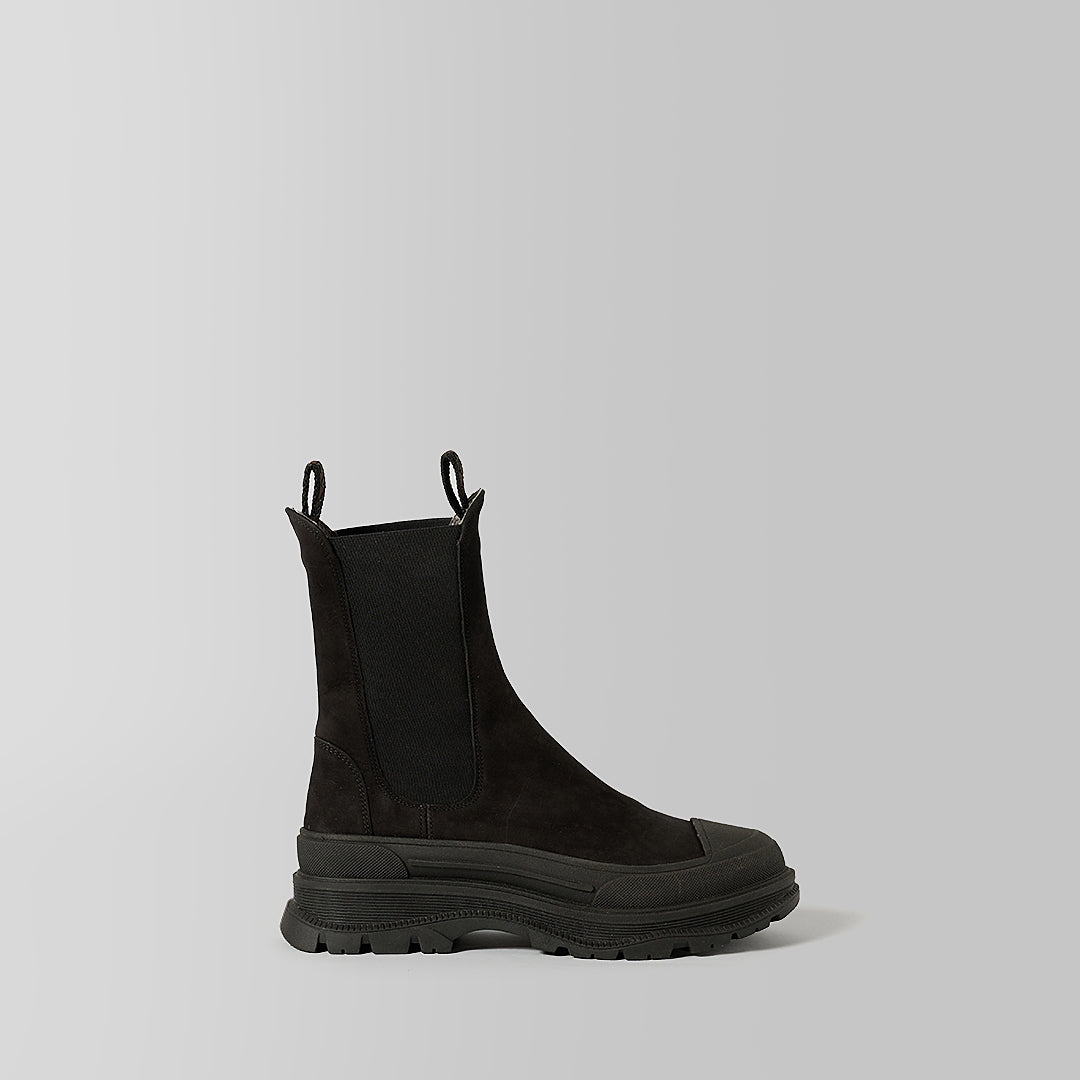 A single black Chelsea-style ankle boot with a chunky lug sole, side gusset, and pull tabs, photographed in profile against a light gray studio background.