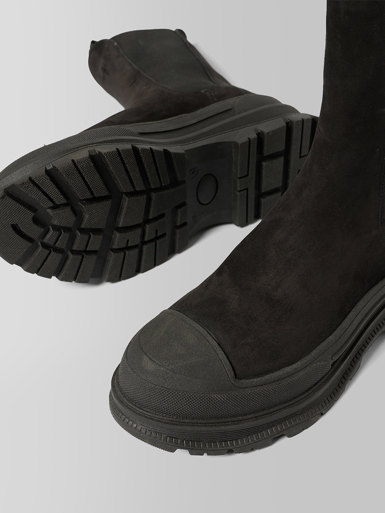 Black suede ankle boots with chunky lug soles, shown from the side and sole detail on a light gray background.