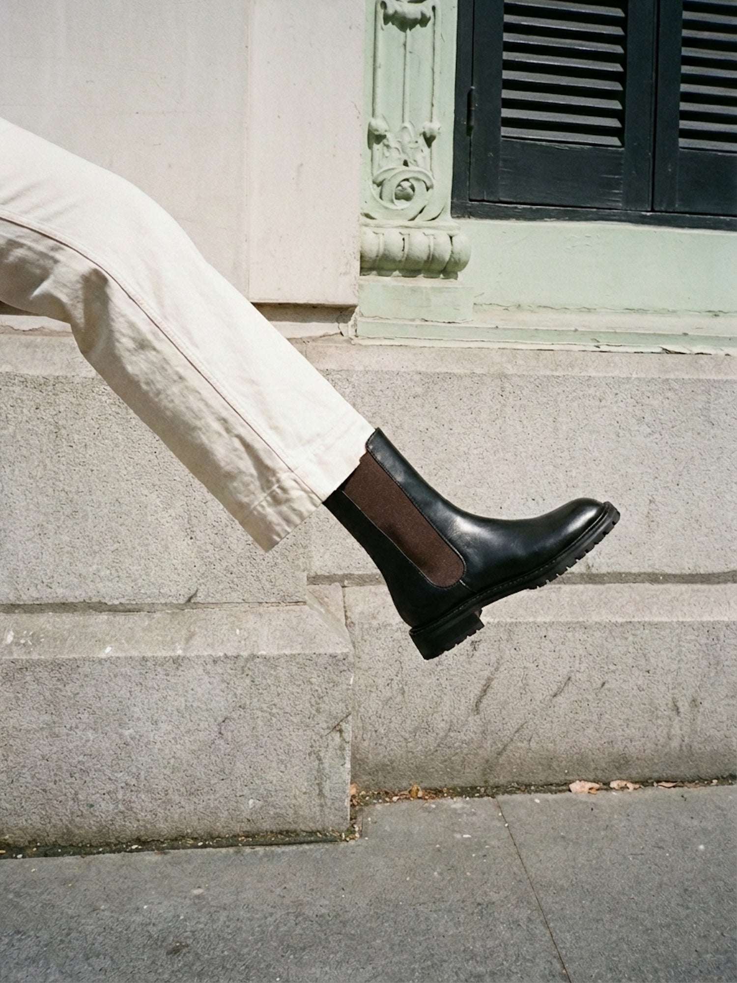 Person wearing black Chelsea boots and light-colored pants sitting on stone steps.