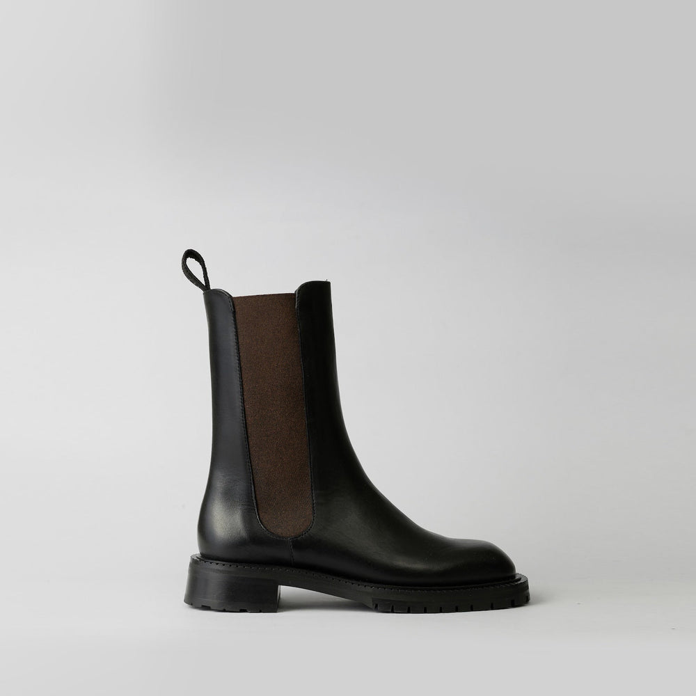 Black Chelsea boot with brown side panel on a light gray background