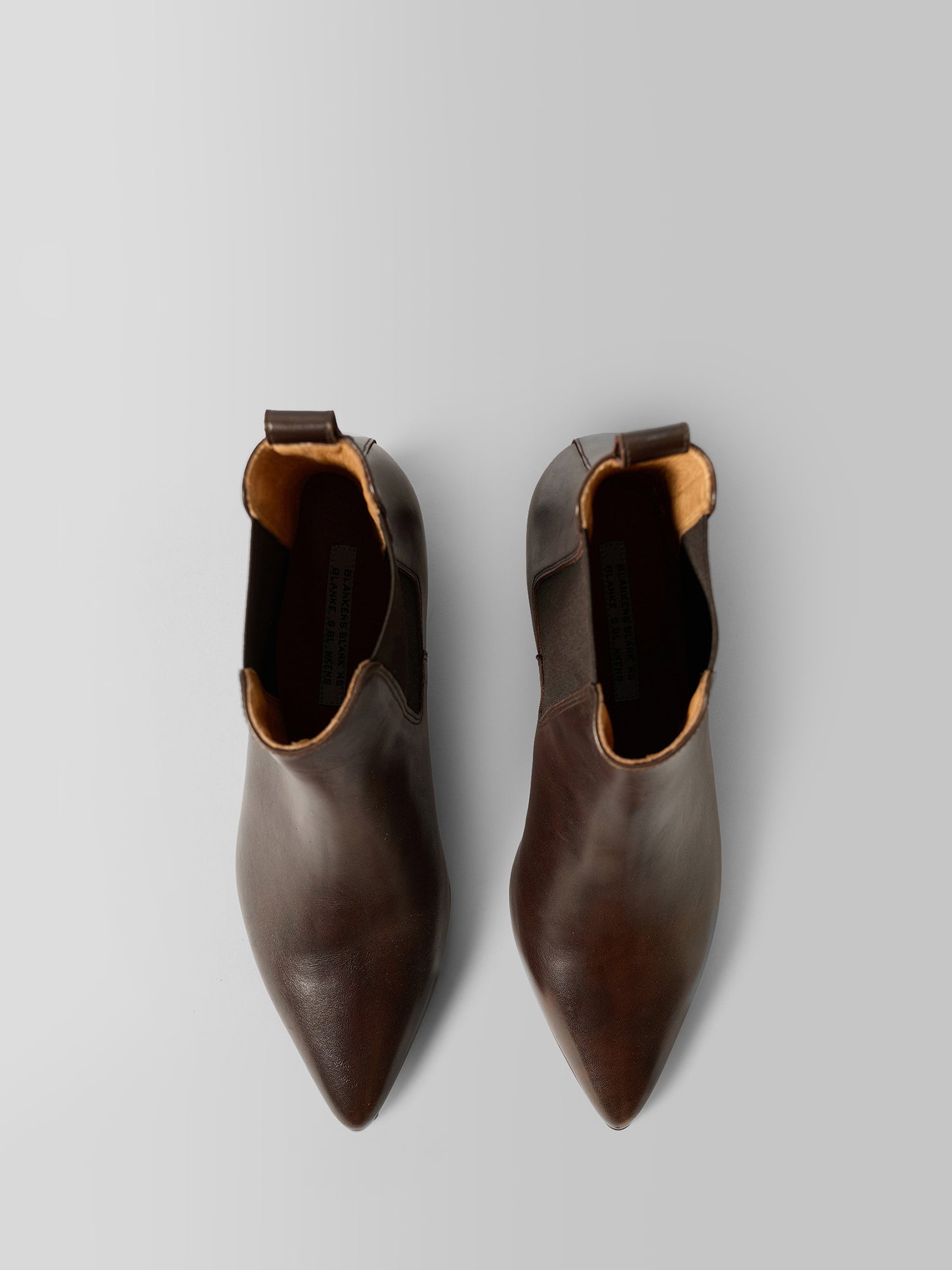 A pair of dark brown leather pointed-toe Chelsea boots shown from a top-down view on a light gray background.