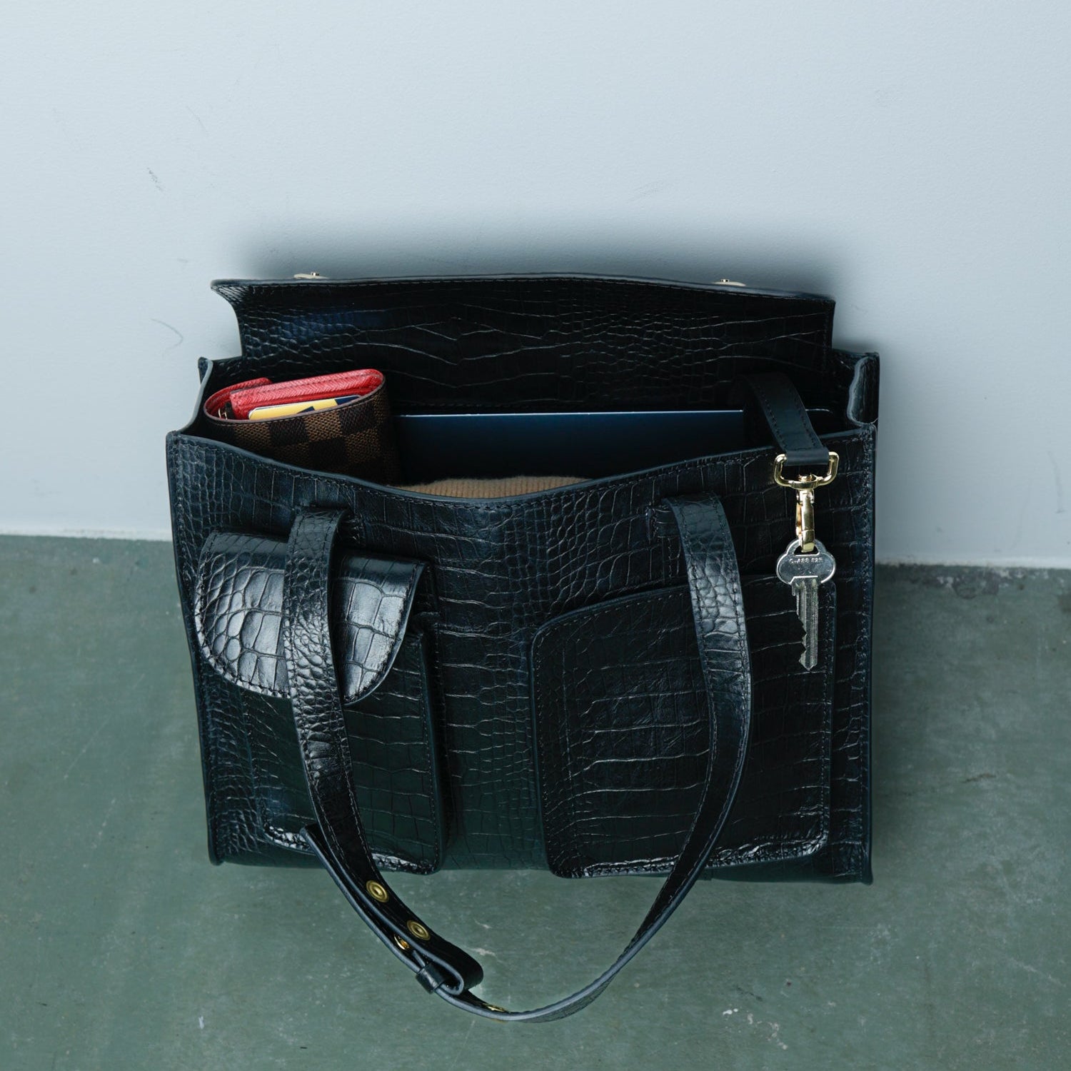 Black textured handbag with a key and phone on a gray surface
