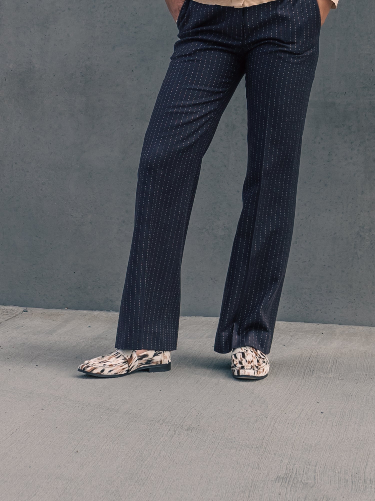 Person wearing dark pinstripe pants and patterned shoes on a gray background